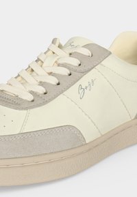 Baskets en cuir crème et gris clair avec lacets blancs et logo « Boss » sur le côté, semelle texturée et détails cousus.