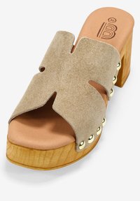 Sandalia de plataforma de gamuza beige con punta abierta, diseño cortado en curvas, tacón de madera y tachuelas metálicas a lo largo del borde exterior. Talla 36.