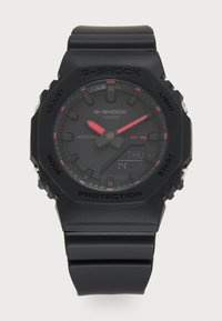 Montre G-SHOCK avec un bracelet et un boîtier en résine noire mate, dotée d'un affichage numérique et analogique avec des accents rouges. Résistante à l'eau jusqu'à 20 bar.
