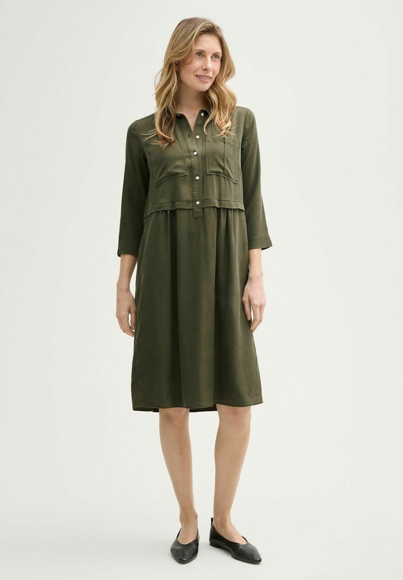 Olivgrünes Kleid mit durchgehender Knopfleiste, zwei Brusttaschen und Dreiviertelärmeln. Weicher Stoff mit lockerer Passform, knielanges Design.
