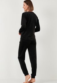 Set van zwarte velours loungewear met een langemouwen top en bijpassende broeken met elastische boorden. Zachte textuur en een ontspannen pasvorm.