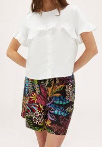 Haut blanc à manches courtes avec un ourlet volanté et un devant à boutons, associé à un short noir arborant des motifs floraux et de feuilles multicolores vibrants.