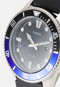 Montre Casio avec un boîtier en acier inoxydable, une lunette noire et bleue, un cadran gris, des index lumineux, et un affichage de la date à 3 heures. Étanchéité 200M.
