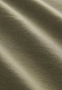 Detail zeleného pleteného materiálu ukazujúci jemnú textúru a mäkké záhyby.