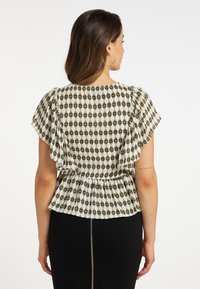 Hvid skjorte med et diamantmønster i sort og guld, med korte voluminøse ærmer og en samlet talje detaljer.