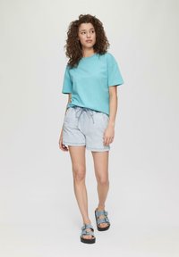 Turkusowy bawełniany T-shirt z krótkimi rękawami, zestawiony z jasnoniebieskimi szortami dżinsowymi z elastycznym pasem i sznurkiem. Niebieskie sandały z klamrami.