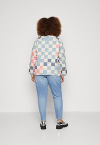 Kurtka pikowana w wielokolorowy kratkowany wzór w jasnym niebieskim, różowym, kremowym i granatowym; zestawiona z jasnymi dżinsami i błyszczącym czarnym obuwiem.