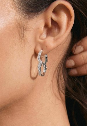 Zilveren oorringen met een golvend ontwerp, voorzien van heldere rhinestones langs één rand voor extra textuur en detail.
