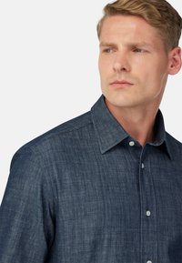 Camicia di jeans scura con colletto classico, caratterizzata da un tessuto testurizzato e bottoni chiari per un contrasto.