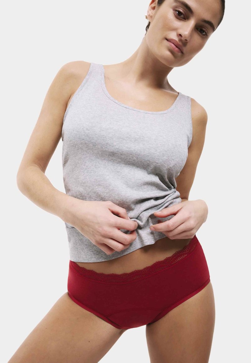 Szary bawełniany top na szerokich ramiączkach oraz czerwone majtki z koronką. Top jest lekko marszczony w talii, podkreślając kolory i faktury.