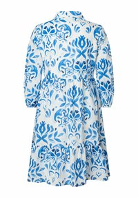 Weißes Kleid mit blauen Blumen- und abstrakten Mustern, mit Kragen, langen Ärmeln und einem rüschierten Saum. Hergestellt aus leichtem Stoff.