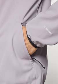 Ελαφρύ μπουφάν λεβάντας με τσέπη που διαθέτει ρυθμιζόμενο κορδόνι, ελαστικές μανσέτες και το λογότυπο "FLASHDRY" σε λευκό στο μανίκι.