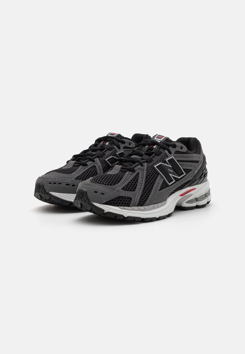 Zapatillas deportivas negras con parte superior de malla, acentos grises, detalles reflectantes y suela de goma con cápsulas de amortiguación. Diseño con cordones y logotipo.
