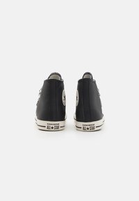 Zapatillas altas negras Converse con suelas de goma blanca, que cuentan con un logo circular en los lados exteriores y un material texturizado.