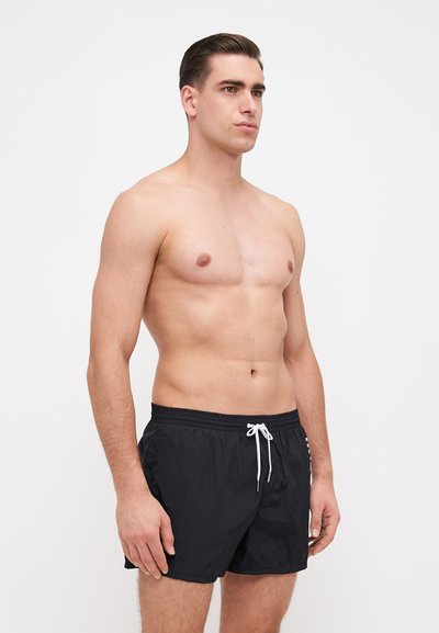 Shorts de bain noirs avec une taille élastique et un cordon blanc. Tissu léger avec une texture lisse, présentant un design simple.