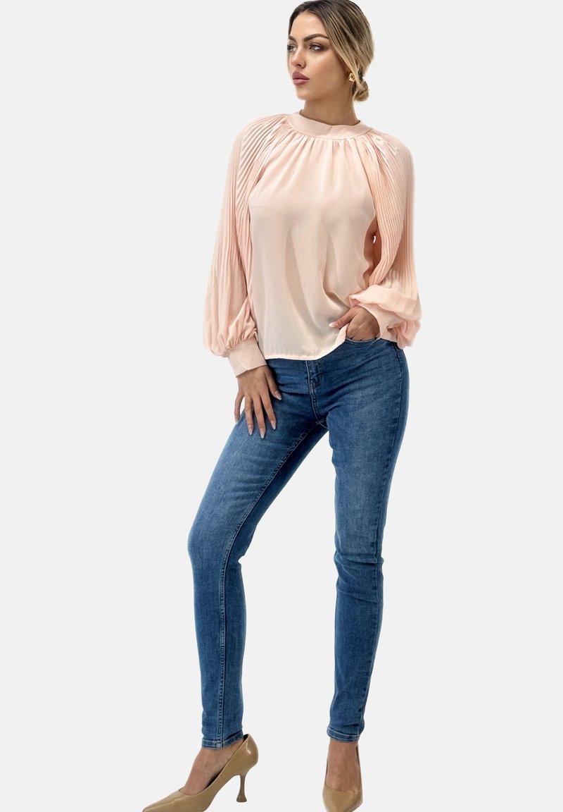 Hellrosa Bluse mit plissierten Schultern, langen puffigen Ärmeln, kombiniert mit blauen Skinny-Jeans und beigefarbenen High Heels. Glatte Textur, lässige Passform.