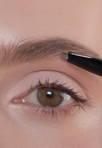 Nahaufnahme eines Augenkontos, das mit einem schwarzen Stift geformt wird, mit natürlicher Brauenstruktur, heller Haut und braunem Auge mit definierten Wimpern.