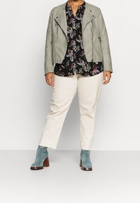 Light gray faux leather jacket over a black paisley print blouse, paired with cream wide-leg pants and teal suede heeled ankle boots.