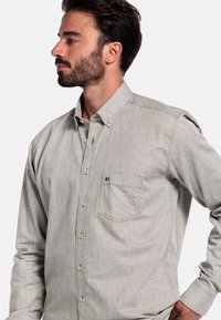 Grijze button-up overhemd gemaakt van textuurstof, met een zijzak, zichtbare stiksels en een kraag met knoopaccenten.