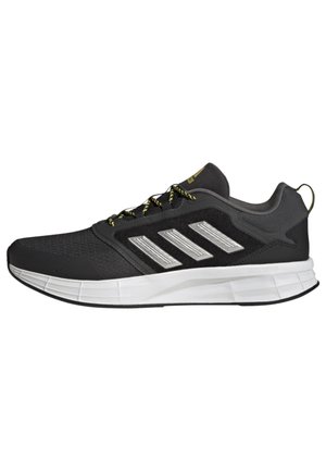 Zapatillas deportivas negras con una parte superior de malla texturizada, detalles plateados y cordones amarillos en contraste. Presentan una suela blanca acolchada.