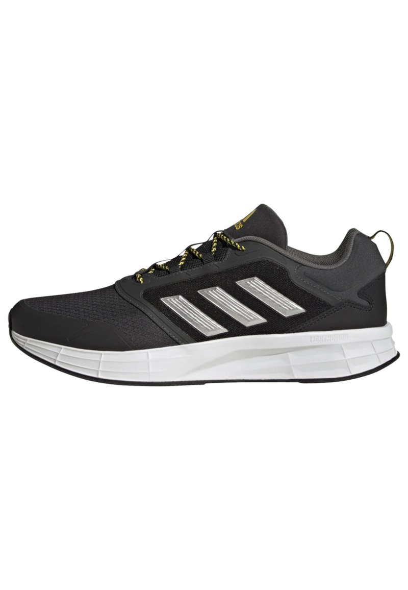Zapatillas deportivas negras con una parte superior de malla texturizada, detalles plateados y cordones amarillos en contraste. Presentan una suela blanca acolchada.