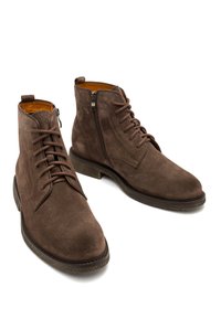 Brązowe zamszowe botki za kostkę z okrągłym noskiem, sznurowaniem z przodu i zamkiem błyskawicznym z boku. Posiadają teksturowaną gumową podeszwę i pomarańczowe skórzane wykończenie wewnętrzne.