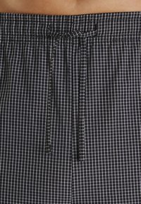 Juodos ir baltos languotos kelnės su raišteliu, surištu į mazgą elastingame juosmenyje, dėvimos žmogaus.