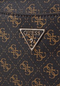 Materiale testurizzato nero con un motivo a logo dorato. Include un logo metallico triangolare argentato con "GUESS USA" all'interno.