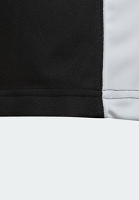 Camiseta deportiva en blanco y negro con textura de malla, destacando un contraste entre las secciones sólidas en negro y blanco, con detalles cosidos visibles.