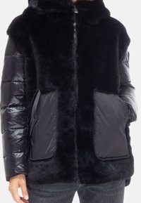 Giacca foderata in pelliccia nera con un design imbottito liscio, dotata di due tasche anteriori e chiusura con zip. Tessuto morbido con cappuccio.