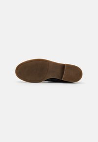 Baskets noires avec une semelle en caoutchouc texturé. La semelle est de couleur marron clair et présente une zone lisse avec une empreinte de logo.