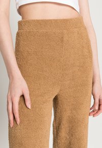 Calças castanhas, texturizadas, com uma aparência suave e felpuda. O design de cintura alta não apresenta fechos ou bolsos visíveis.