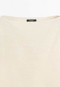 Close-up van een crèmekleurige kledinghals met een zwart label waarop "Massimo Dutti" en "Made in China." staan