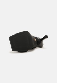Chaussure à talons hauts noire avec un bout carré et un talon fin vue du côté de la semelle sur fond blanc.