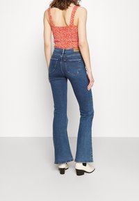 Cropped top rosso a fiori con scollo quadrato abbinato a jeans a vita alta blu a campana. Materiale: denim. Scarpe: stivali bianchi alla caviglia con tacco basso.