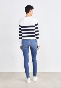 Witte en marineblauwe gestreepte trui met een ronde halslijn, gecombineerd met blauwe skinny jeans. De outfit wordt afgewerkt met witte sneakers.