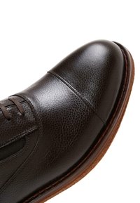 Dunkelbraunes Lederschuh mit strukturiertem Obermaterial, runder Zehenpartie und sichtbarem Schnürsenkel. Mit einer kontrastierenden braunen Sohle und minimalen N�ähdetails.