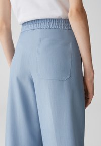 Pantalons à taille élastique bleu clair avec une poche arrière, présentant une texture lisse et un design à jambe droite.