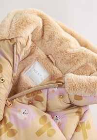 Gefüttertes Innenfutter des Mantels aus weichem, beigem Kunstfell. Außen bietet der Mantel einen hellbraunen Stoff mit verspielten Blumen- und Pflanzenmustern in Rosa und Gold.