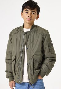 Grüne Bomberjacke, gepolstertes Material, gerippte Bündchen, Reißverschluss und Druckknopfverschluss, zwei Seitentaschen und ein Patch-Detail am linken Arm.