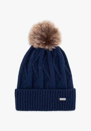 Marineblauwe gebreide muts met een gestructureerd kabelpatroon en een lichtbruine nepbont pompon bovenop; voorzien van een klein merketiket aan de zijkant.