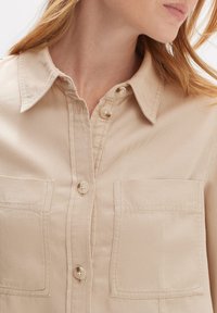 Beige overhemden van geweven katoen-twill, met twee borstzakken en een klassieke kraag. Subtiele textuur zichtbaar in de stof.