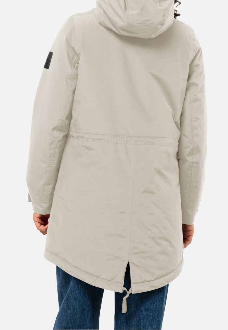 Světle béžová parková bunda s kapucí, vybavená stahovací šňůrou v dolní části, postranním rozparkem a černou nášivkou loga na levém rukávu. Vyrobena z texturovaného, voděodolného materiálu.