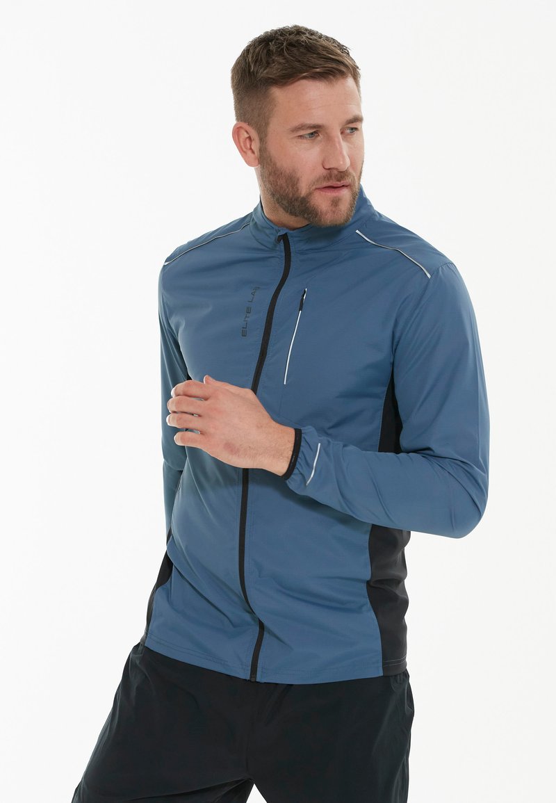 Leichte blaue Sportjacke mit hohem Kragen, Frontreißverschluss, schwarzen seitlichen Einsätzen, reflektierenden Akzenten und einer mit Reißverschluss versehenen Brusttasche.