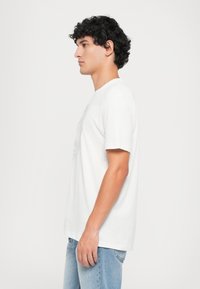 Hvitt bomull T-skjorte med korte ermer, rund halslinning, og grafisk trykk på forsiden. Kombinert med lyseblå denim jeans.