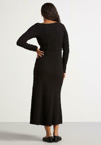 Svart långärmad klänning med en texturerad, krinklad tyg; kroppsnära silhuett som sträcker sig till midjan; rund halsringning med en mjuk yta.