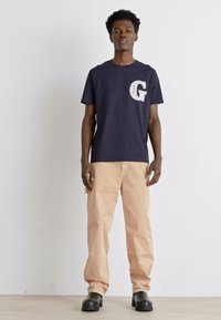 Camiseta de algodón de color navy con el logo blanco "G" en el lado izquierdo del pecho, combinada con pantalones rectos de color beige claro y botas negras de caña alta.