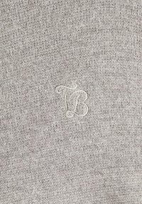 Šedá pletenina s jemným vyšívaným logom v jemnej bielej farbe. Textúra je hladká s jemným vzorom pleteniny.