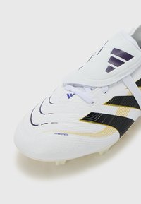 White soccer cleat featuring a textured synthetic upper with black and gold accents, a secured lace system, and a distinct curved shape.