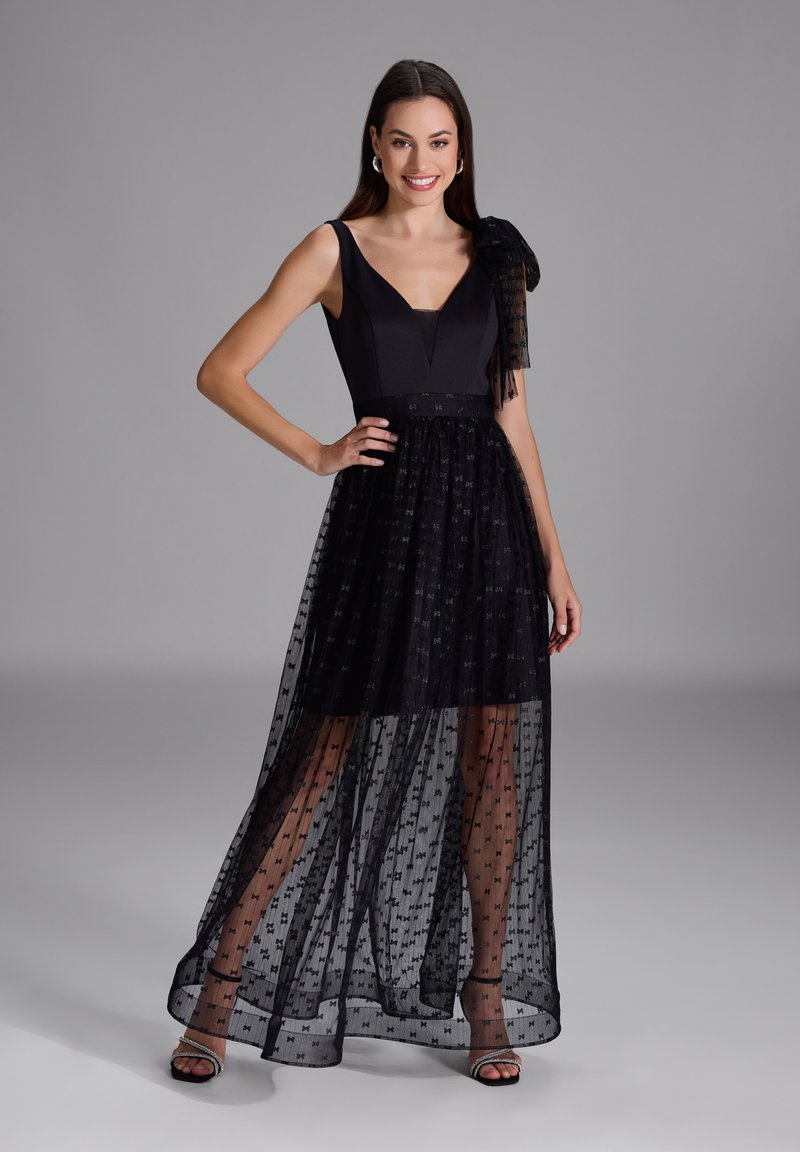 Robe noire avec un corsage ajusté, jupe en couches transparentes avec des motifs d'étoiles, bretelle réglable et chaussures à talons ouverts.